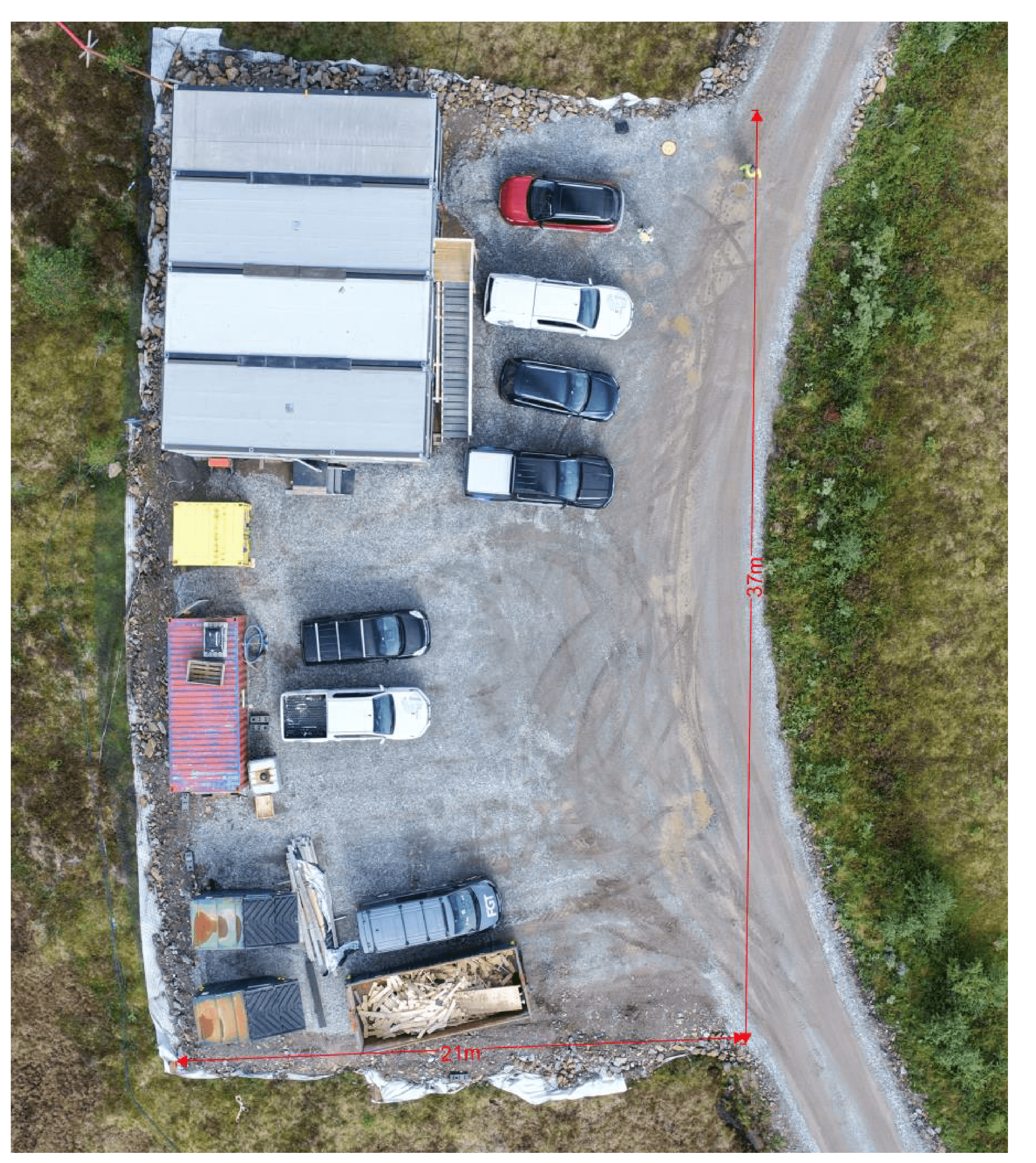 Dronefoto rett ovenfra av gruslagt riggplass ved dam Samsjøen med parkerte biler, brakke og containere. Røde målpiler viser 21 og 37 meter.