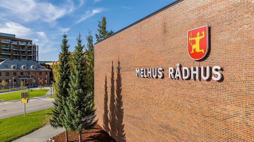 Melhus rådhus – rød teglfasade med kommunevåpenet og skiltet «MELHUS RÅDHUS».