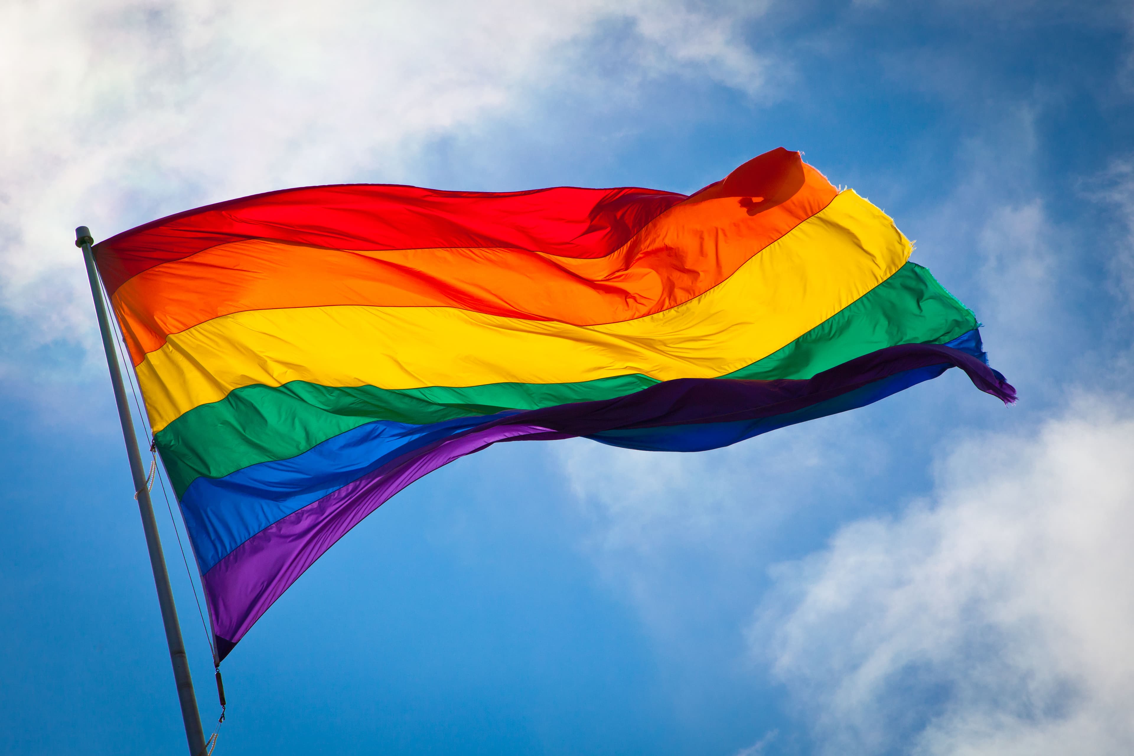 Regnbueflagg (Pride-flagg) som blafrer i vinden mot blå himmel.