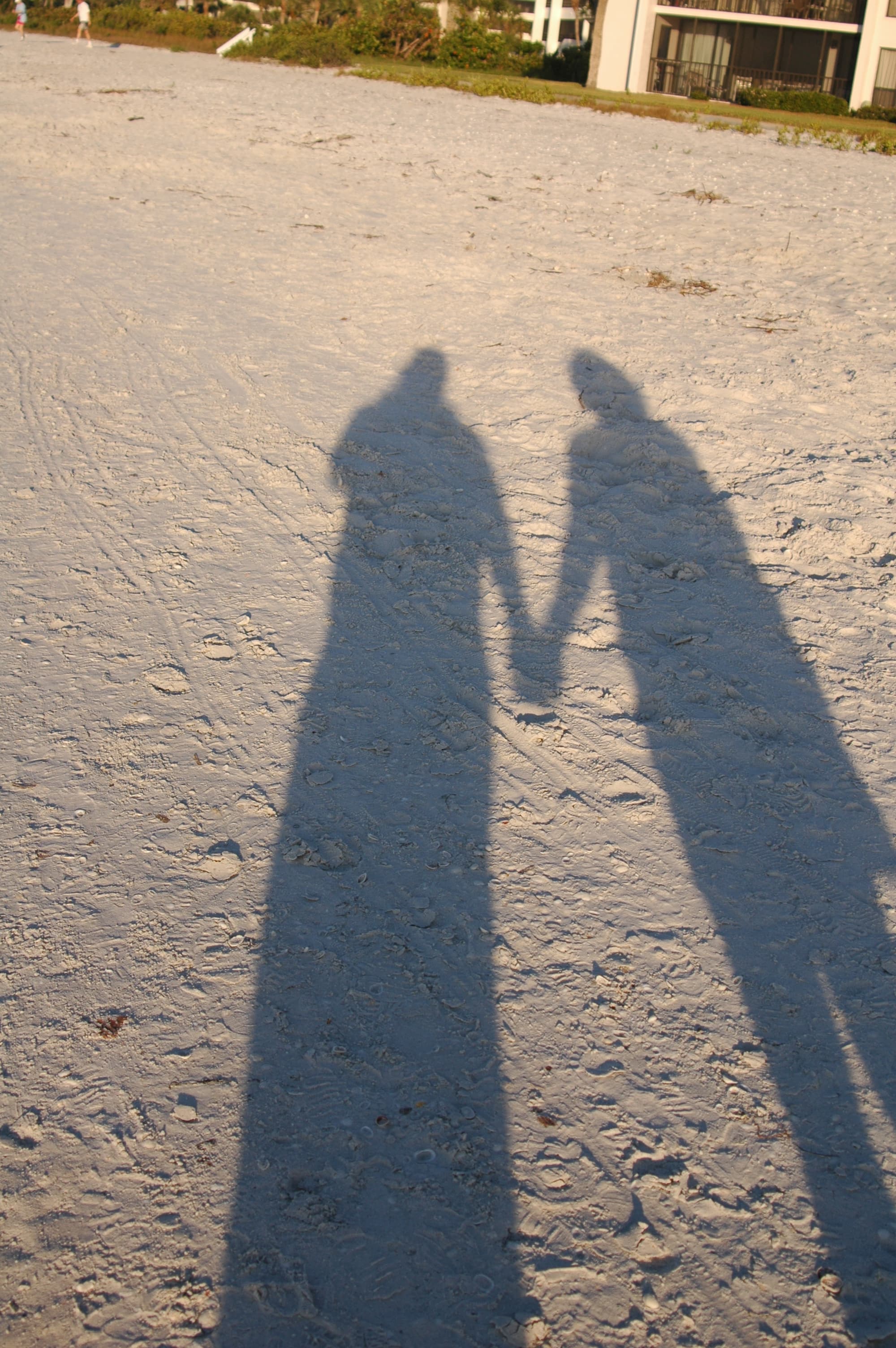 Skyggene av to personer som holder hverandre i hånden, kastet på lys sand – illustrasjonsfoto.