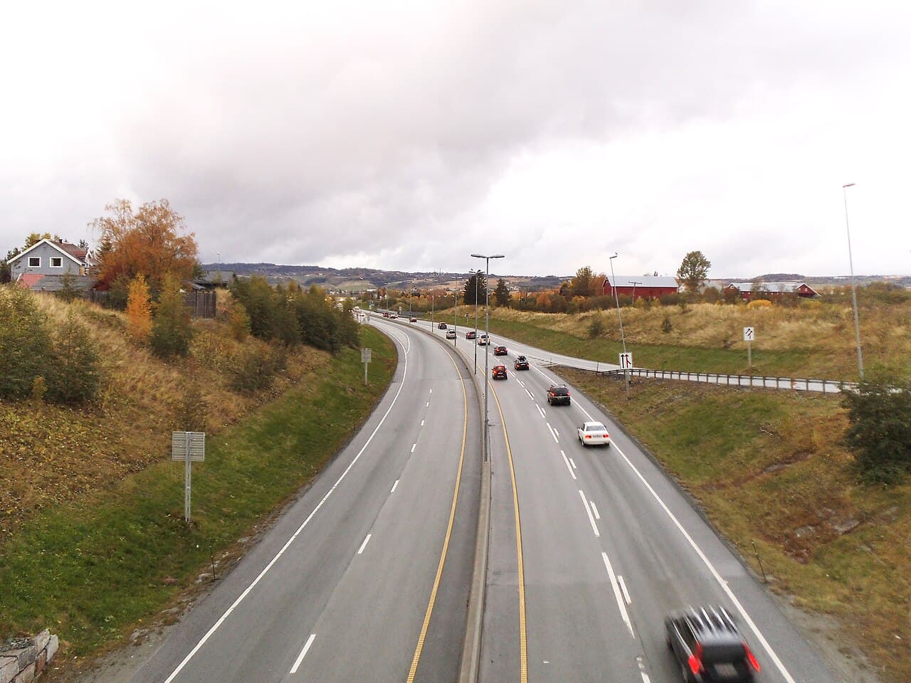 E6 gjennom Melhus sett nordover fra ei bru, med trafikk i begge retninger en overskyet høstdag